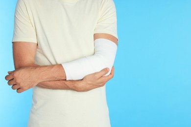 Photo of Man with arm wrapped in medical bandage on light blue background, closeup. Space for text