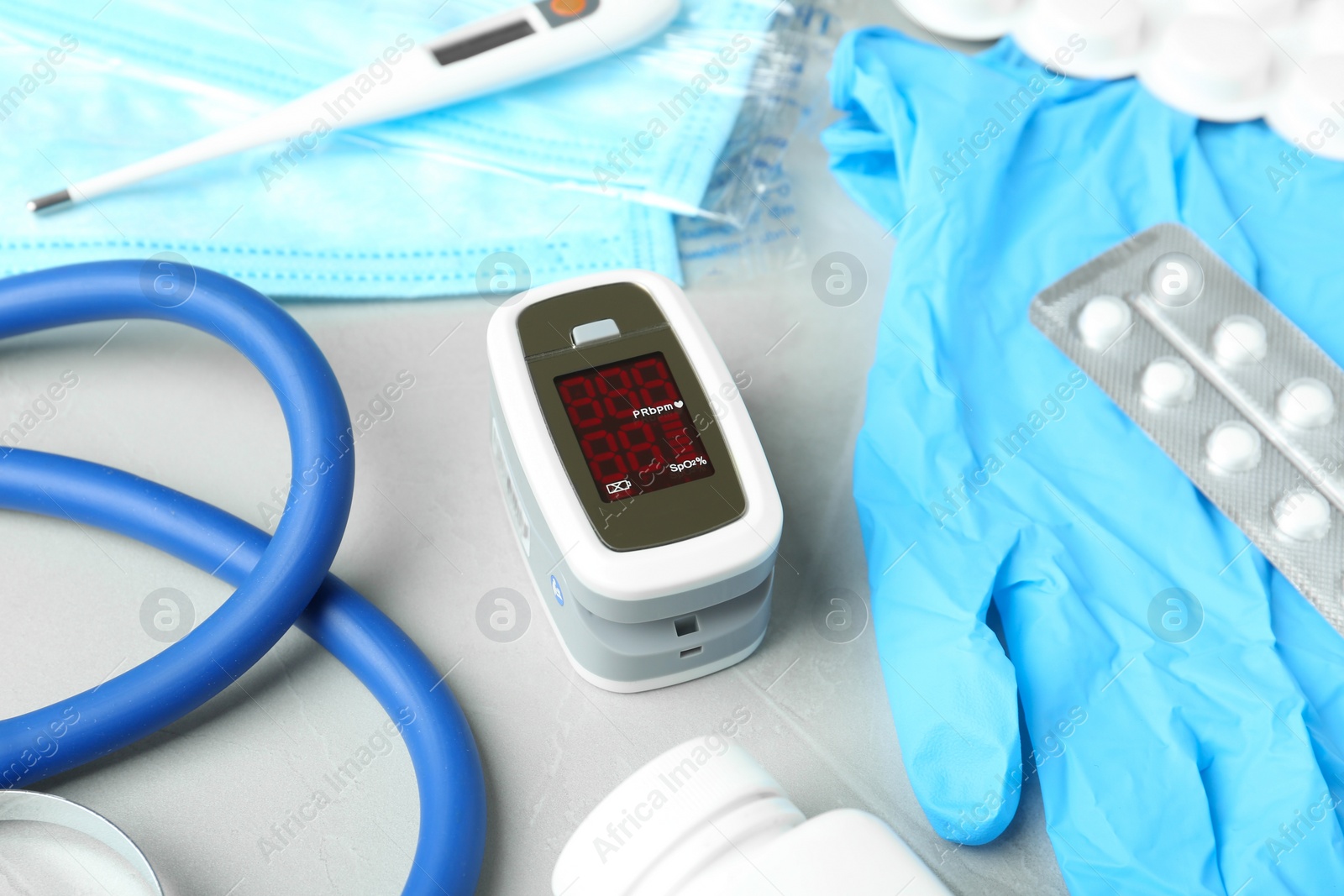 Photo of Modern fingertip pulse oximeter and medical items on light grey stone background