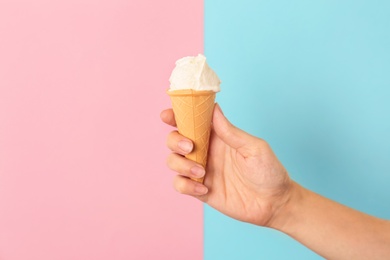 Photo of Woman holding waffle cone with tasty vanilla ice cream on color background