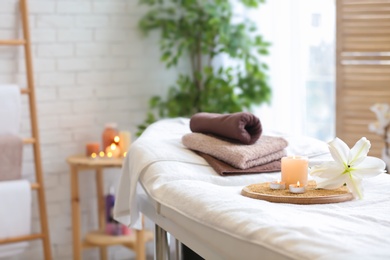 Photo of Towels, candles and flower on massage table in spa salon