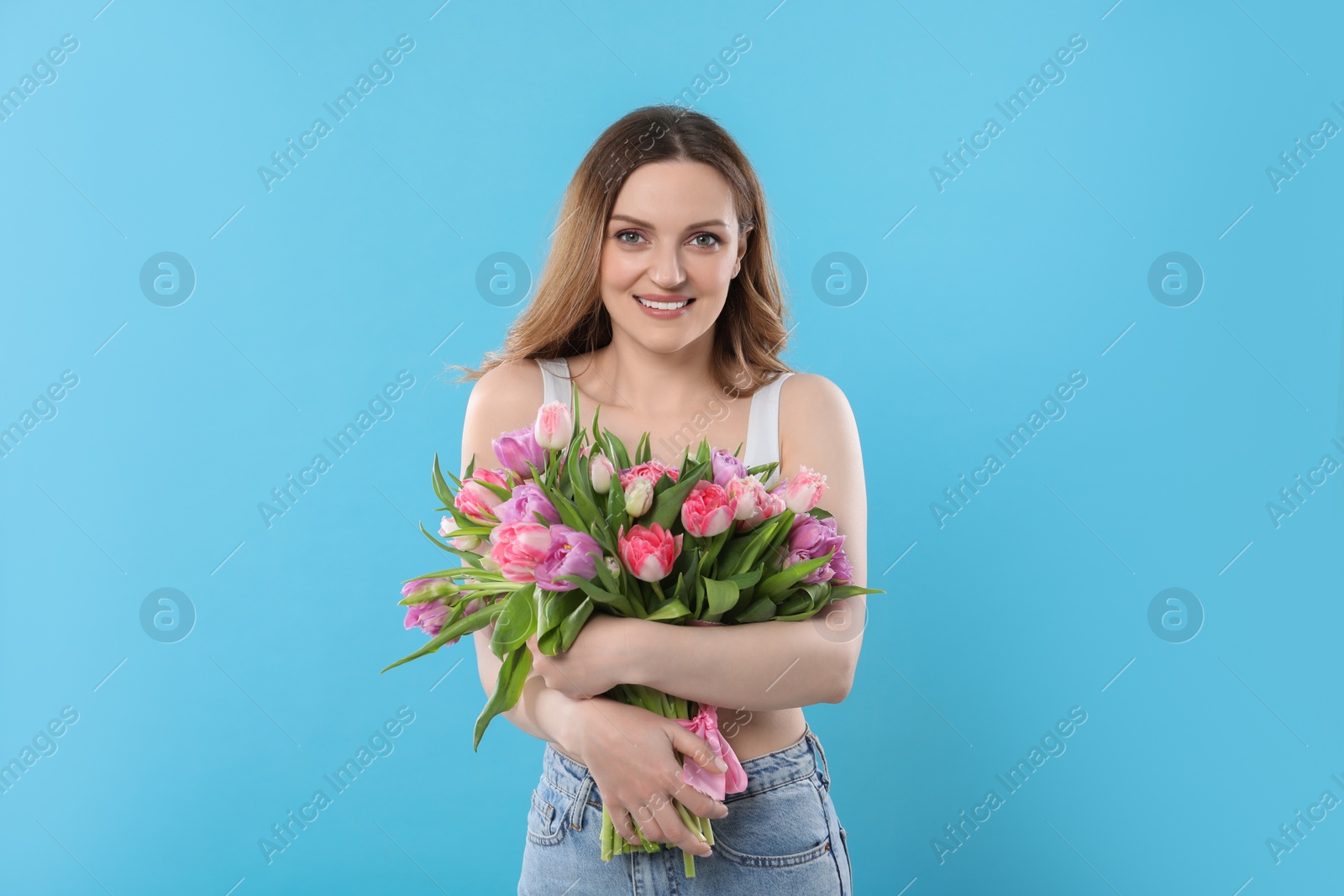 Photo of Happy young woman with bouquet of beautiful tulips on light blue background