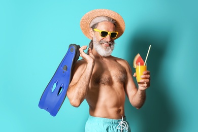 Shirtless man with glass of cocktail and flippers on color background