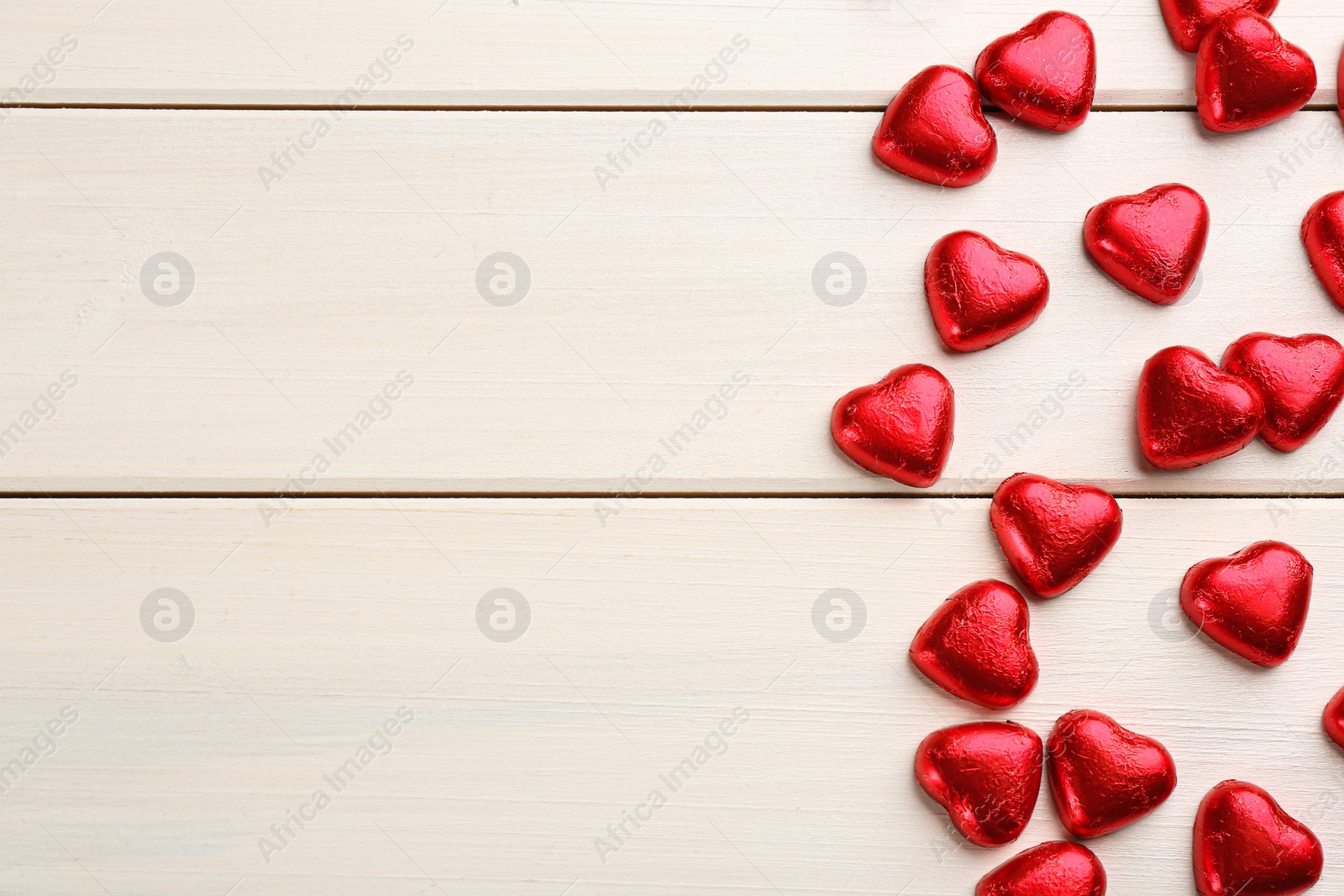 Photo of Heart shaped chocolate candies on white wooden table, flat lay. Space for text