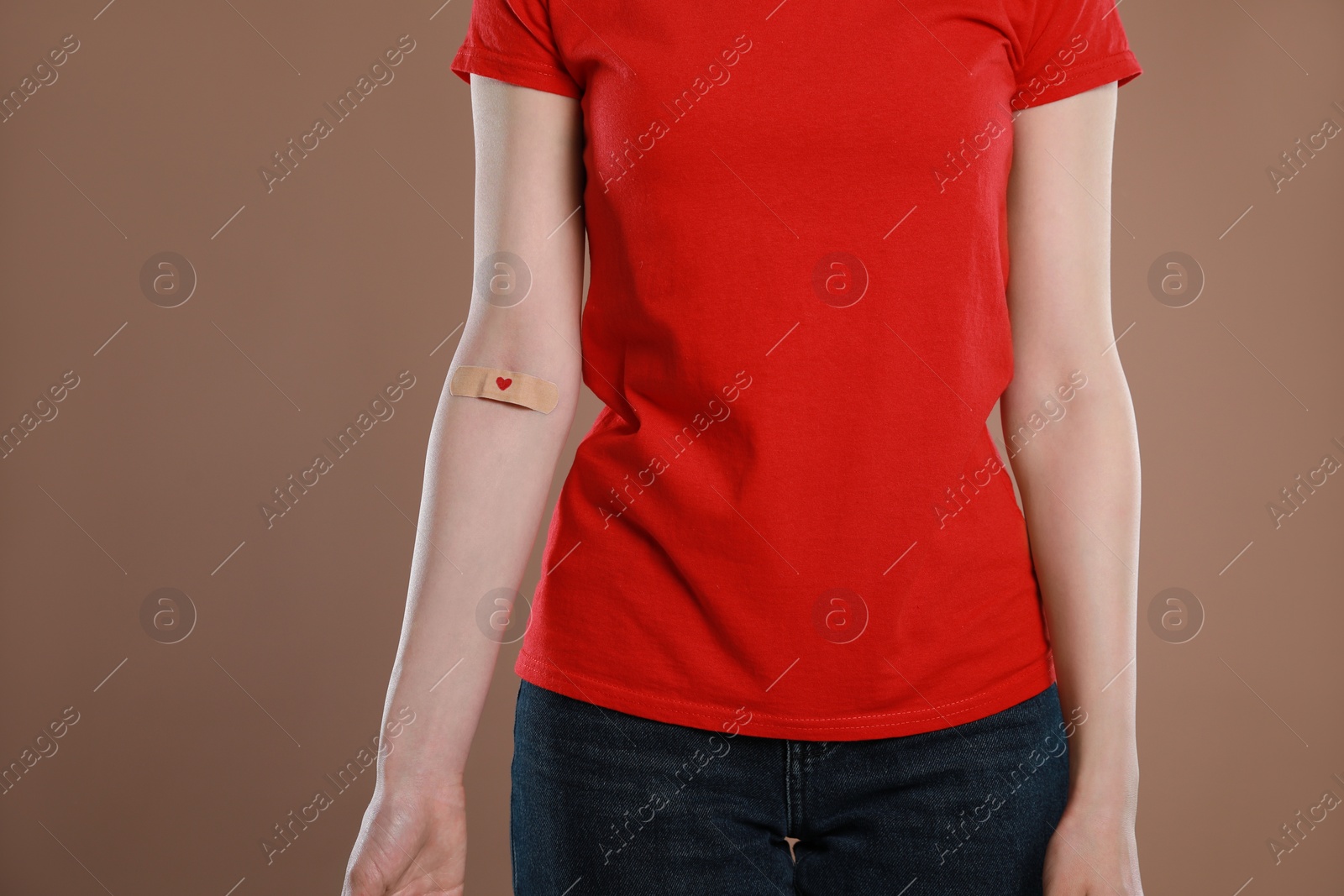 Photo of Blood donation concept. Woman with adhesive plaster on arm against brown background, closeup. Space for text