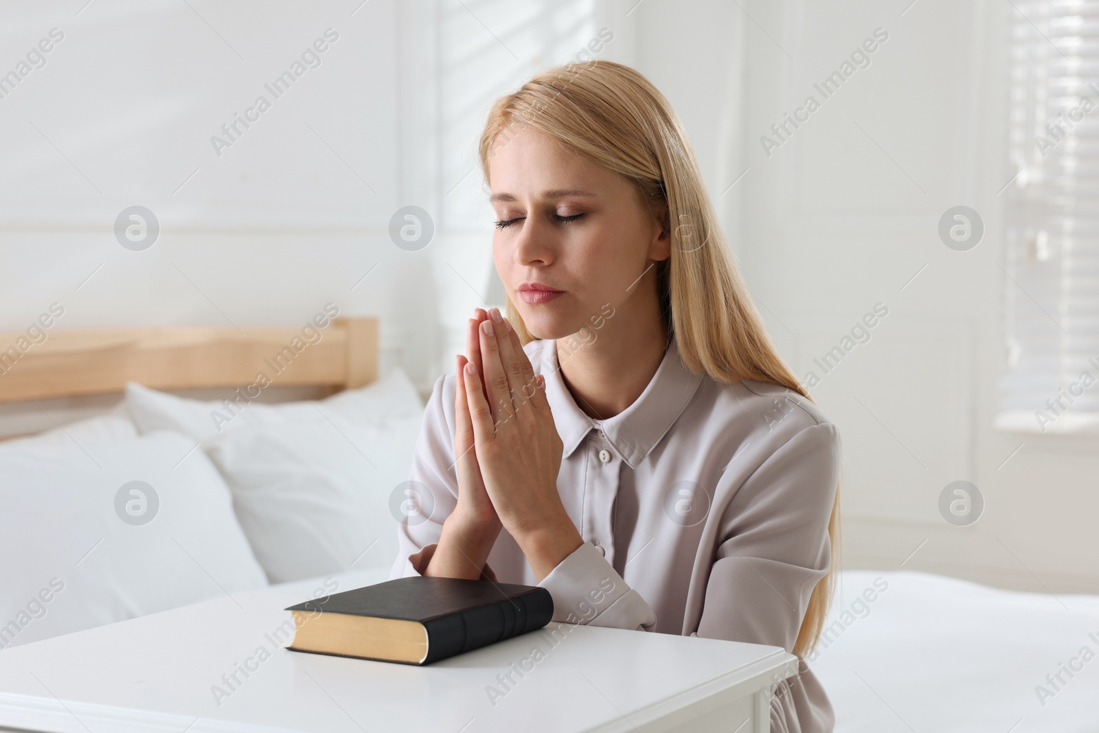 Photo of Religious young woman with Bible praying in bedroom