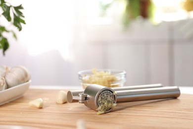 Photo of Garlic press, cloves and mince on wooden table in kitchen