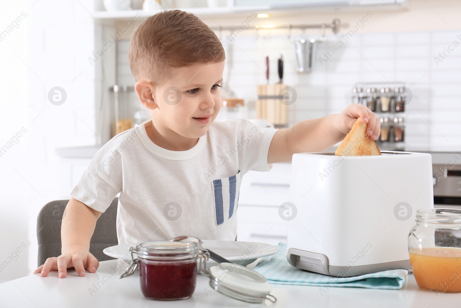 Photo of Cute little boy preparing toast with sweet jam at table
