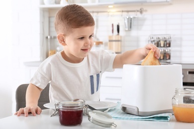 Photo of Cute little boy preparing toast with sweet jam at table