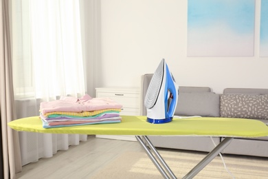 Photo of Board with modern iron and clean laundry at home