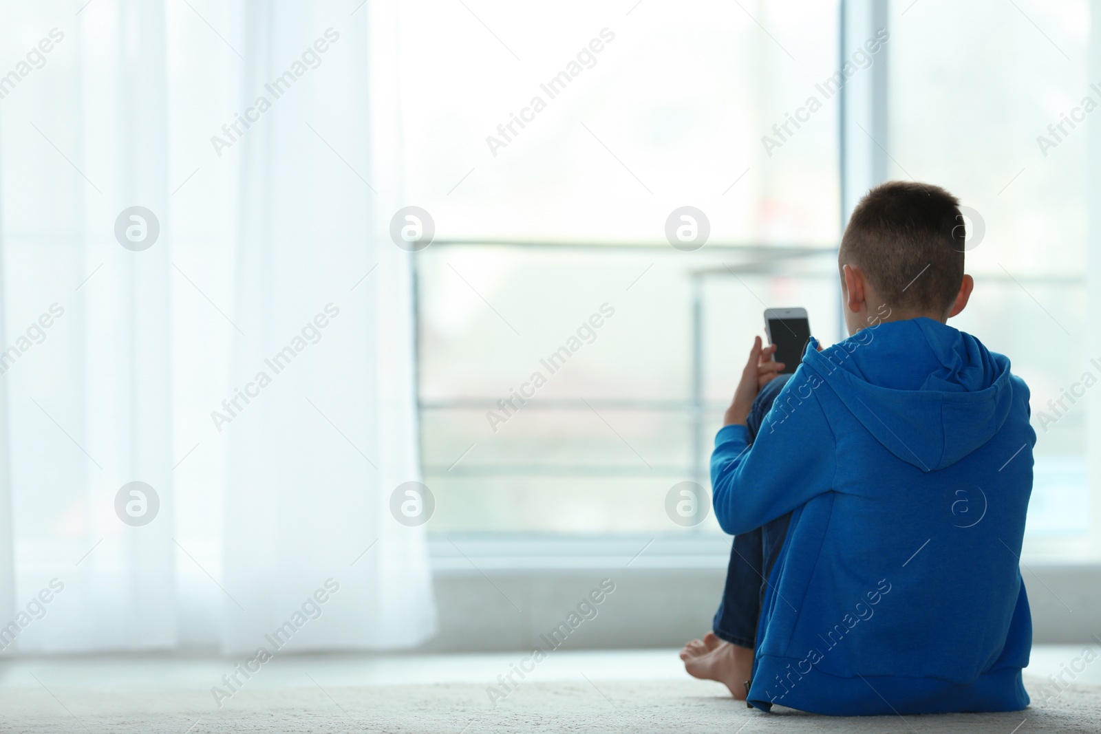 Photo of Upset boy with smartphone sitting near window indoors. Space for text