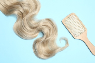 Lock of blonde wavy hair and brush on color background, flat lay