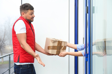 Photo of Emotional courier giving damaged cardboard box to client outdoors. Poor quality delivery service