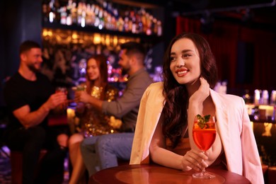 Friends spending time together in bar. Beautiful woman with fresh alcoholic cocktail at table, space for text