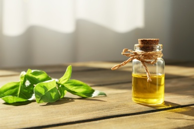 Photo of Bottle of essential basil oil on table against blurred background. Space for text