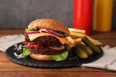 Tasty cheeseburger with patties, French fries and pickles on wooden table, closeup