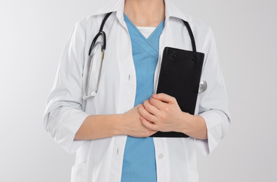 Photo of Doctor with stethoscope and clipboard on light grey background, closeup