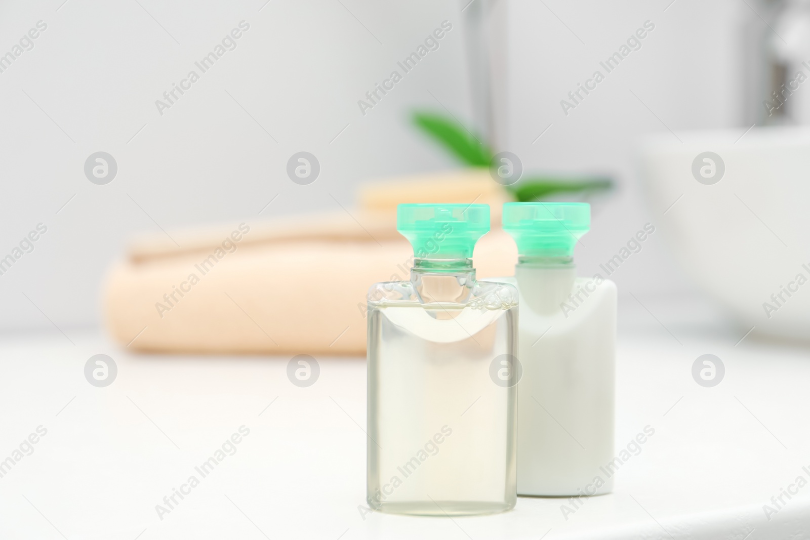 Photo of Mini bottles of cosmetic products on white table against blurred background. Space for text