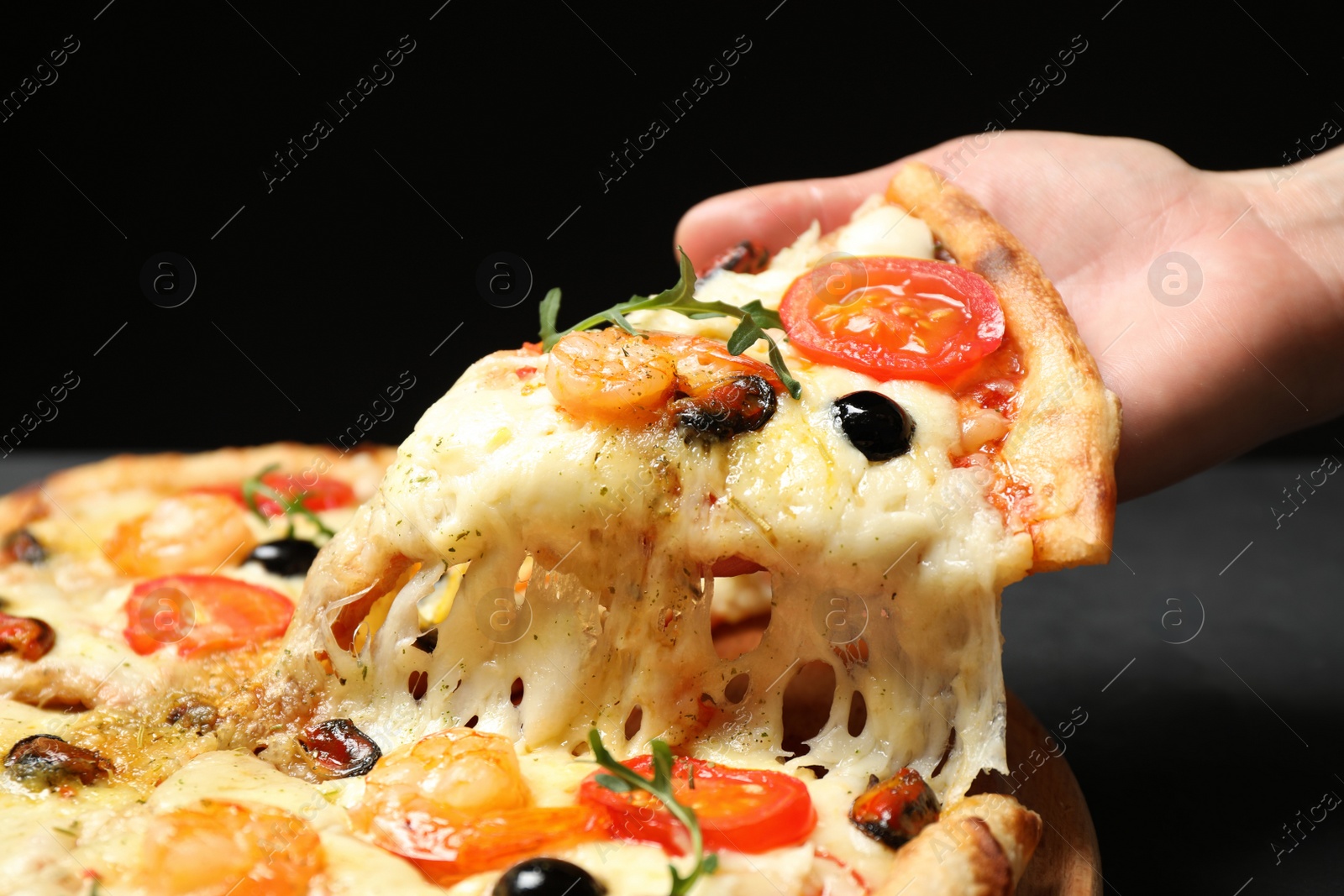 Photo of Woman taking slice of cheese pizza with seafood at table, closeup