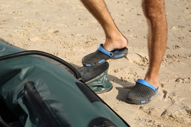 Man pumping inflatable rubber fishing boat at sandy beach on sunny day, closeup