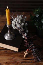 Rosary beads, Bible, burning candle and willow branches on wooden table