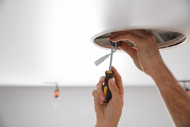 Photo of Worker installing lamp on stretch ceiling indoors, closeup