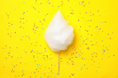 Photo of Stick with yummy cotton candy and sprinkles on color background, top view