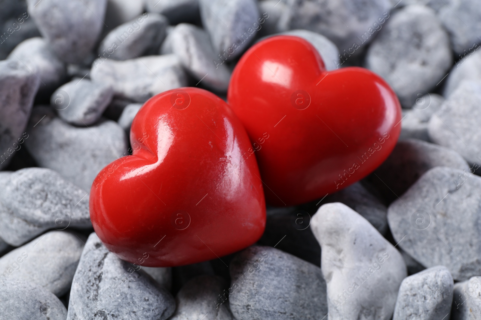 Photo of Red decorative hearts on grey stones, closeup