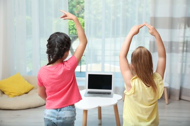 Cute little girls taking online dance class indoors, back view