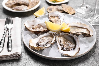 Photo of Fresh oysters with lemon and ice on grey table, closeup