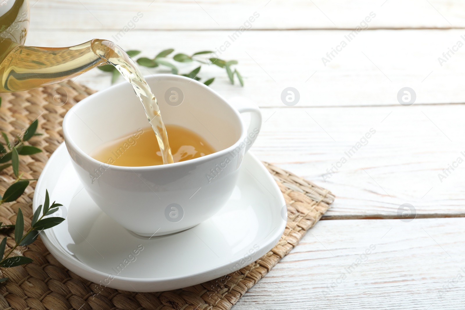 Photo of Pouring aromatic eucalyptus tea into cup on white wooden table. Space for text