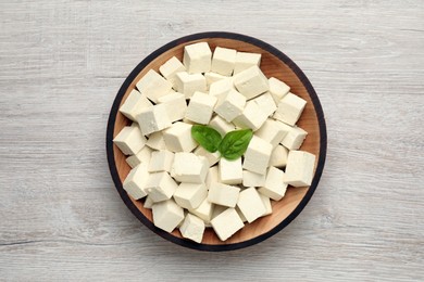 Delicious tofu with basil on light wooden table, top view