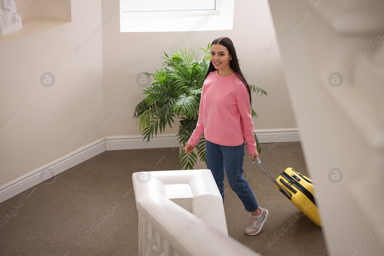 Photo of Beautiful young woman with suitcase going up stairs in hotel