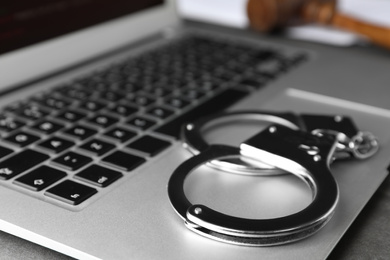 Photo of Laptop and handcuffs on table, closeup. Cyber crime
