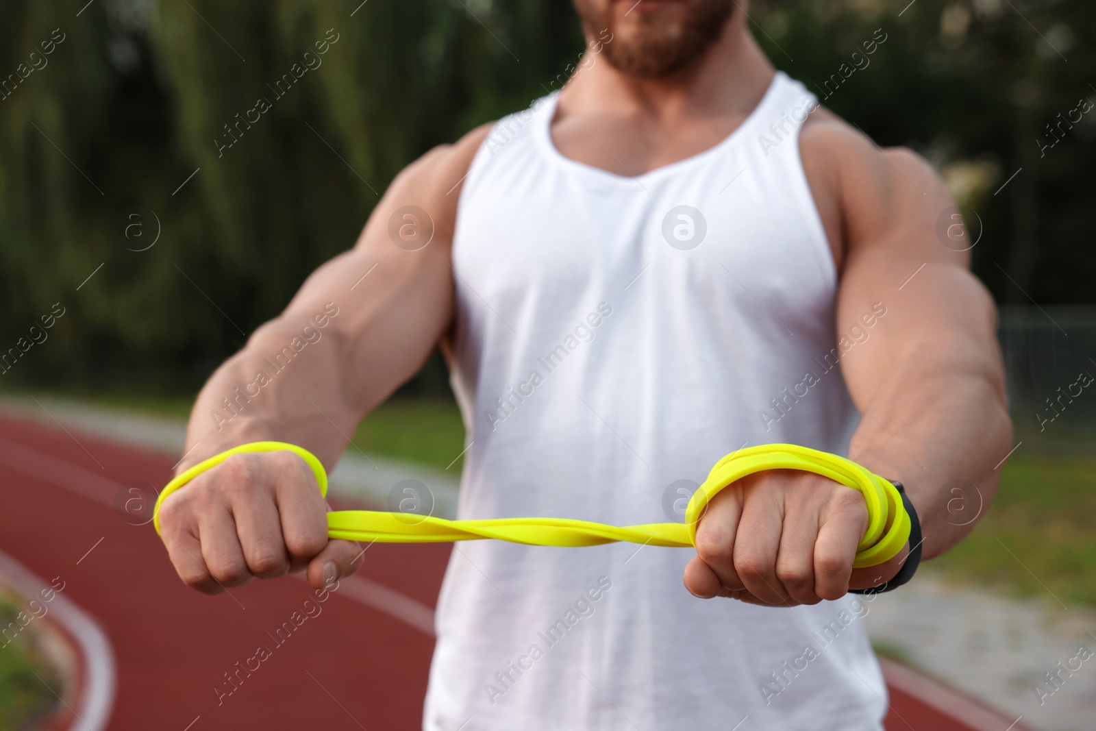 Photo of Muscular man doing exercise with elastic resistance band at stadium, closeup