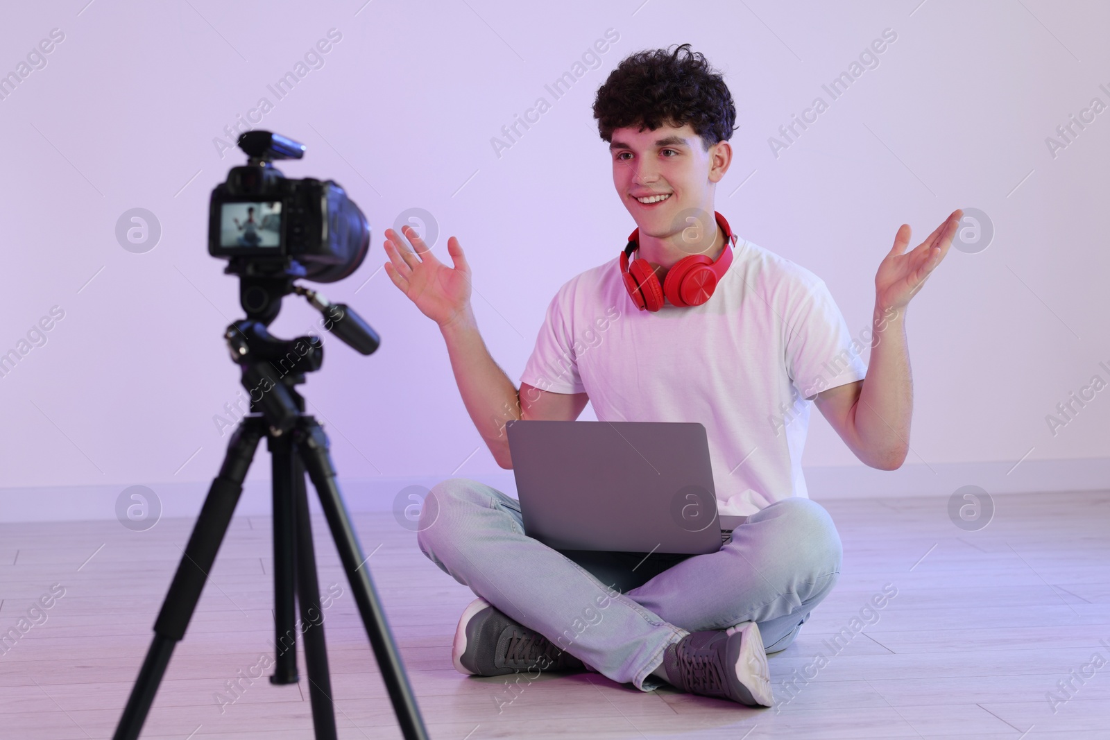 Photo of Smiling teenage blogger with laptop explaining something while streaming indoors
