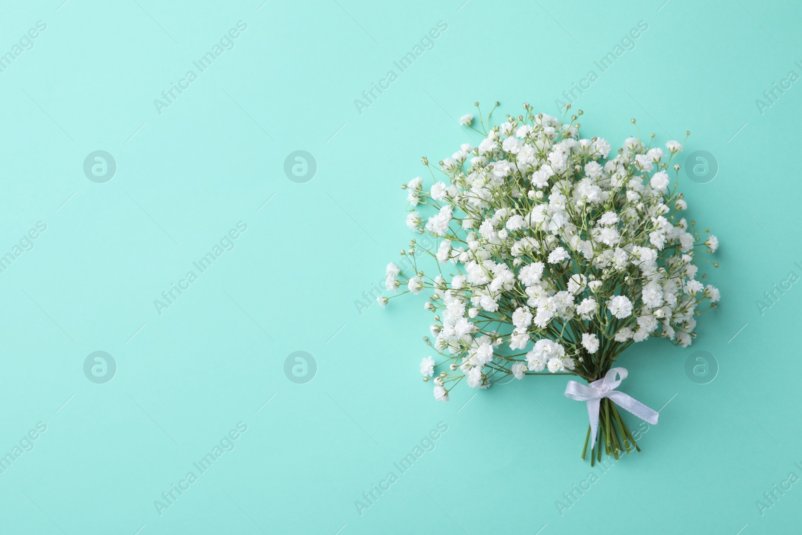 Photo of Beautiful gypsophila flowers tied with ribbon on turquoise background, top view. Space for text