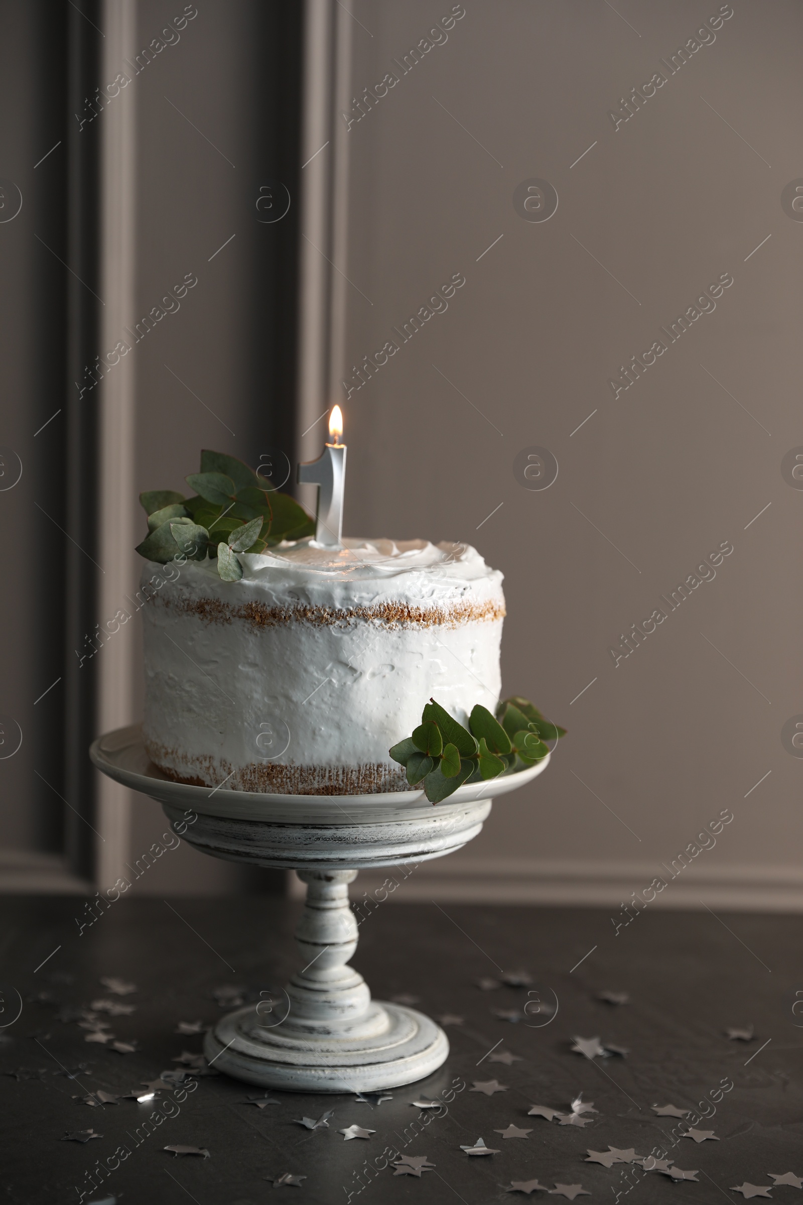 Photo of Tasty Birthday cake with burning candle and eucalyptus branches on grey table