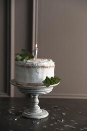 Photo of Tasty Birthday cake with burning candle and eucalyptus branches on grey table