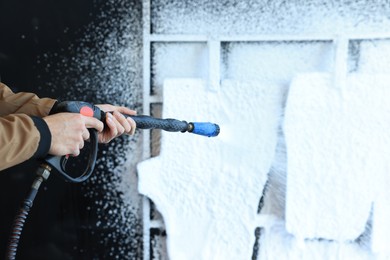 Man cleaning auto mats with high pressure foam jet at self-service car wash, closeup