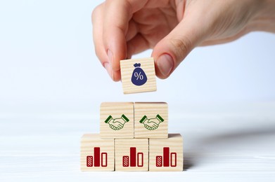 Image of Woman putting cube with percent sign on other ones with charts and illustrations of handshaking on white table, closeup