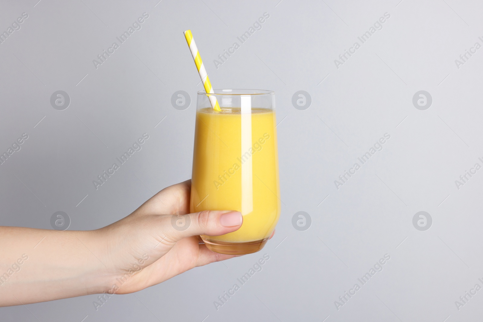 Photo of Woman holding glass of tasty smoothie on light grey background, closeup