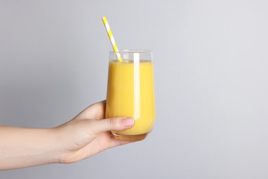 Woman holding glass of tasty smoothie on light grey background, closeup