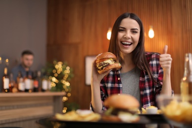 Young woman eating tasty burger in cafe