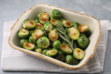 Delicious roasted Brussels sprouts and rosemary in baking dish on grey table