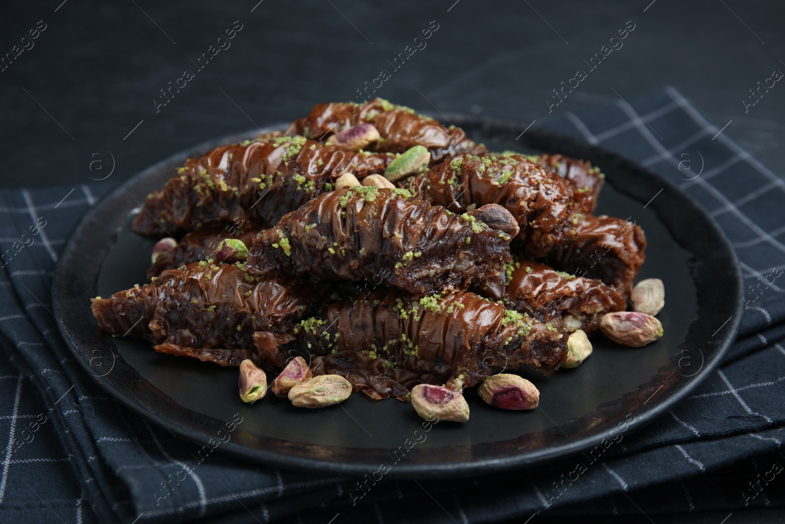 Photo of Delicious baklava with pistachio nuts and napkin on black table, closeup