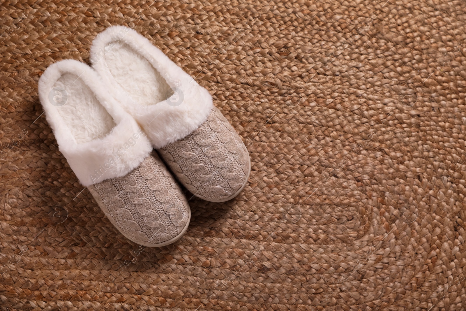 Photo of Pair of warm stylish slippers on wicker carpet, top view. Space for text