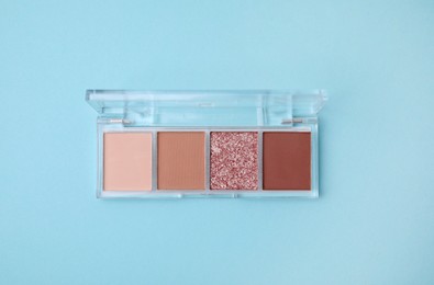 Photo of Beautiful eye shadow palette on light blue background, top view