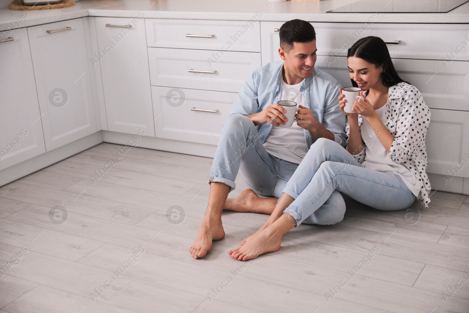 Photo of Happy couple sitting on warm floor in kitchen. Heating system