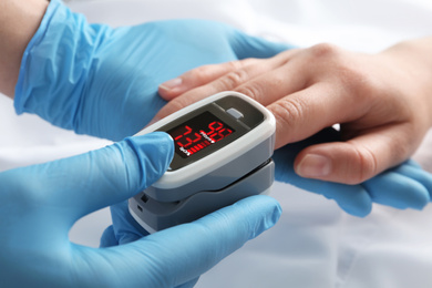 Doctor examining patient with modern fingertip pulse oximeter in bed, closeup