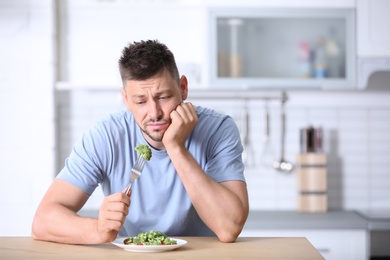 Photo of Portrait of unhappy man eating broccoli salad in kitchen